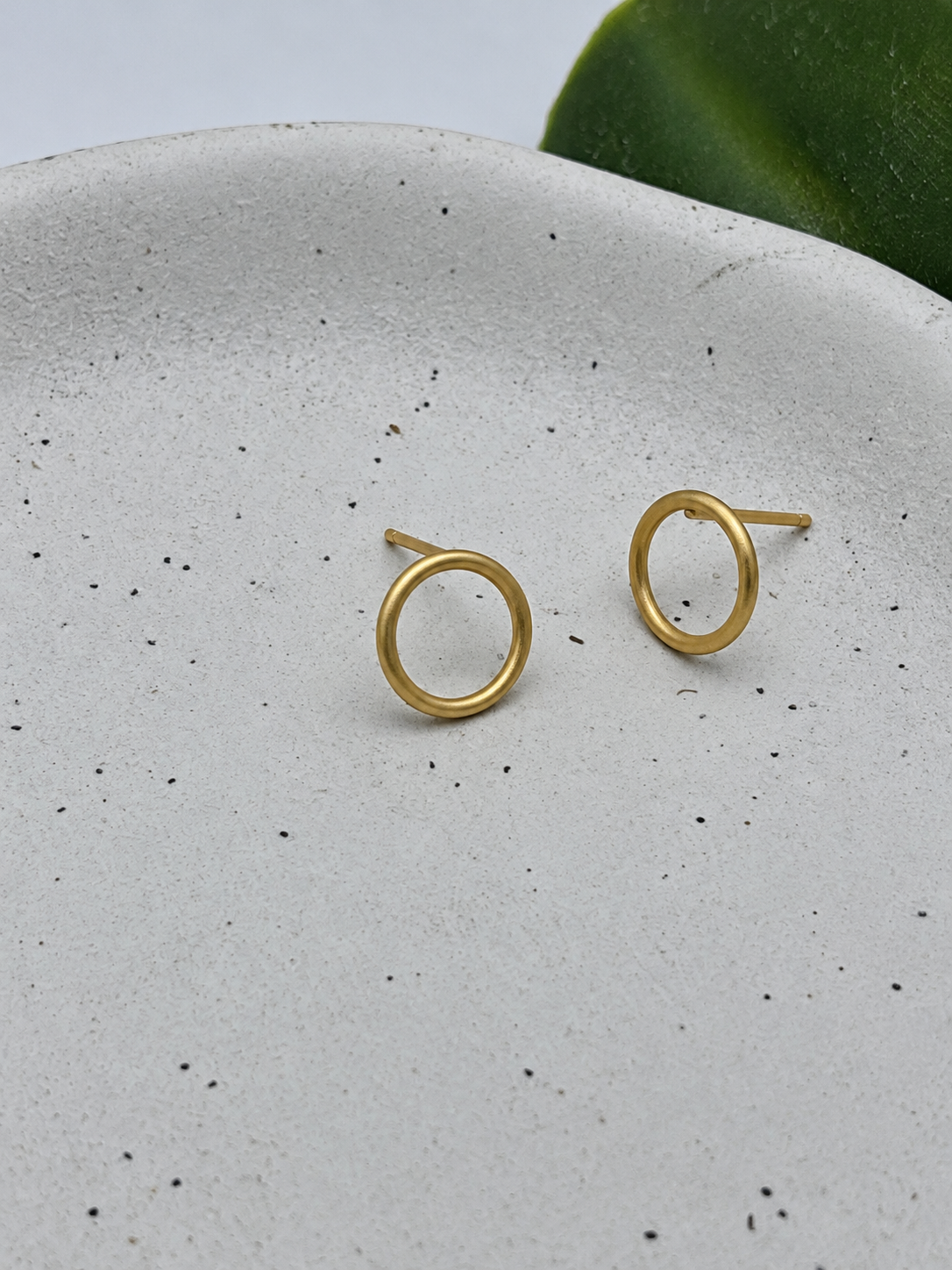 Gold circle stud earrings with a smooth rounded finish, handcrafted by Wild One Jewellery and photographed on a pale speckled ceramic dish.
