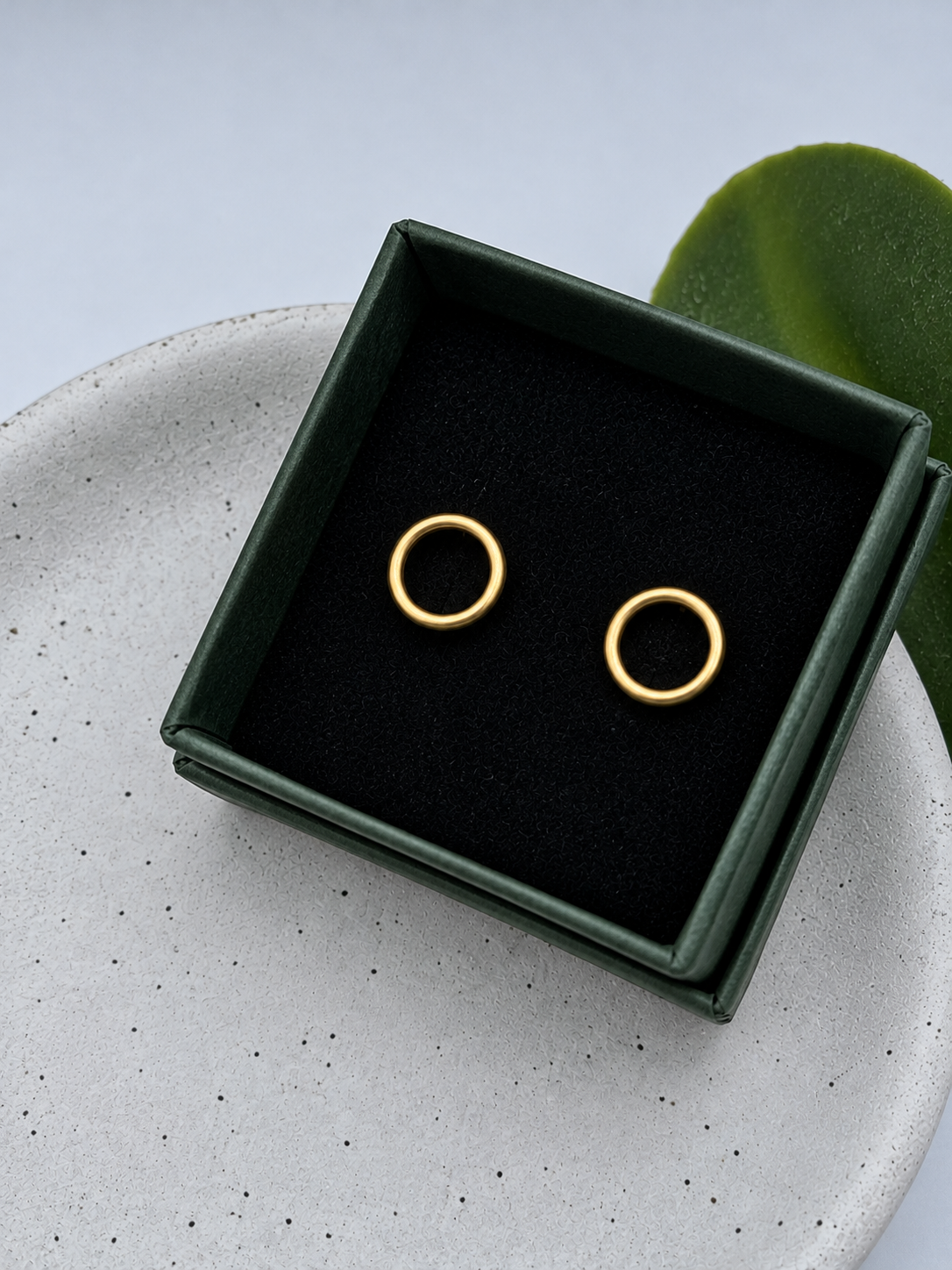 Gold circle stud earrings with a smooth rounded finish, handcrafted by Wild One Jewellery and photographed on a pale speckled ceramic dish.