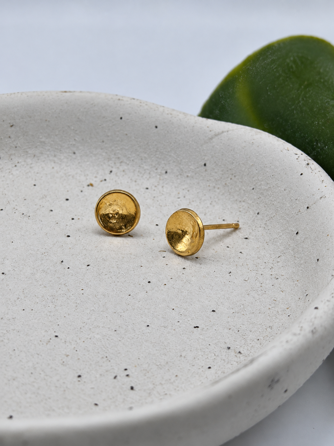 9ct gold New Moon stud earrings with a softly hammered, textured finish and reflective golden surface, photographed on a pale speckled ceramic dish by Wild One Jewellery.