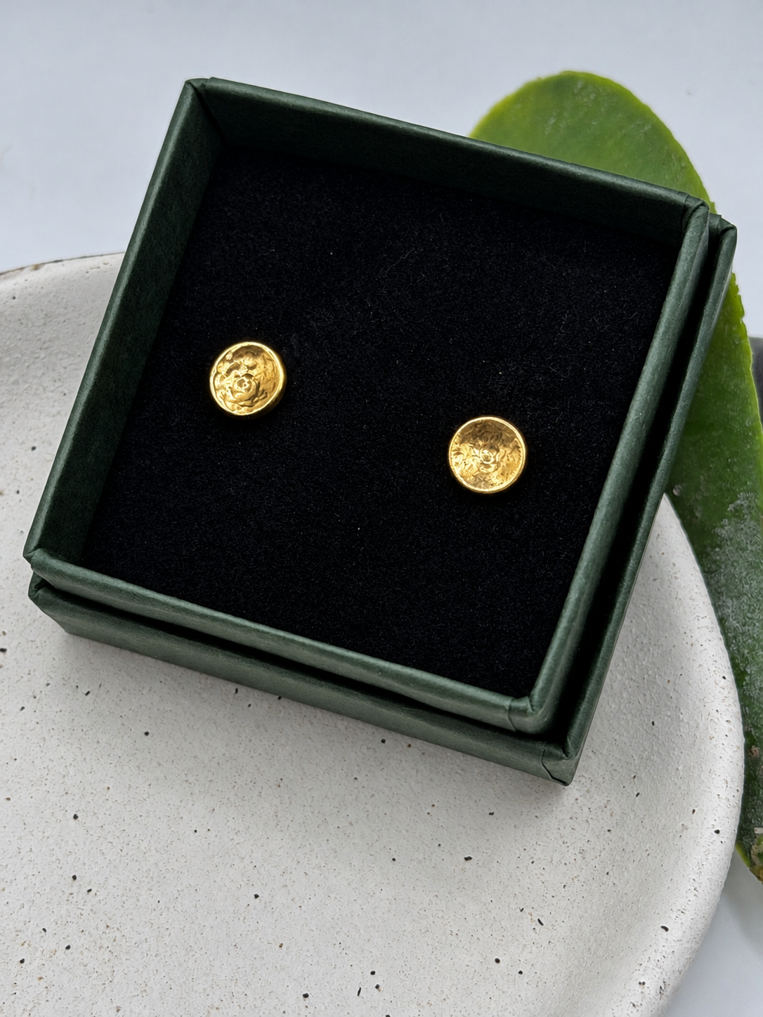 9ct gold New Moon stud earrings with a softly hammered, textured finish and reflective golden surface, photographed on a pale speckled ceramic dish by Wild One Jewellery.