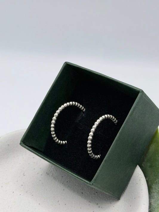 Handmade recycled sterling silver bobble hoop earrings featuring rounded bead detailing, photographed in a dark green jewellery box by Wild One Jewellery, an independent silversmith based in Lincolnshire, UK.