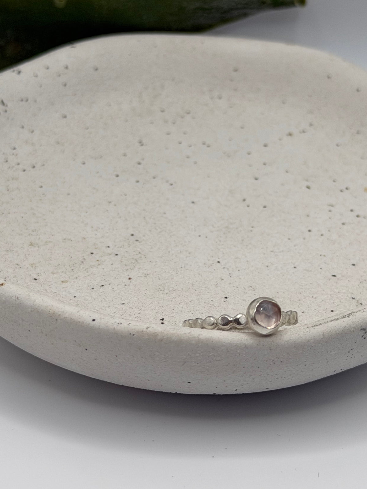 Mini faceted rose quartz ring with a pale pink gemstone set on a textured sterling silver pebble band.