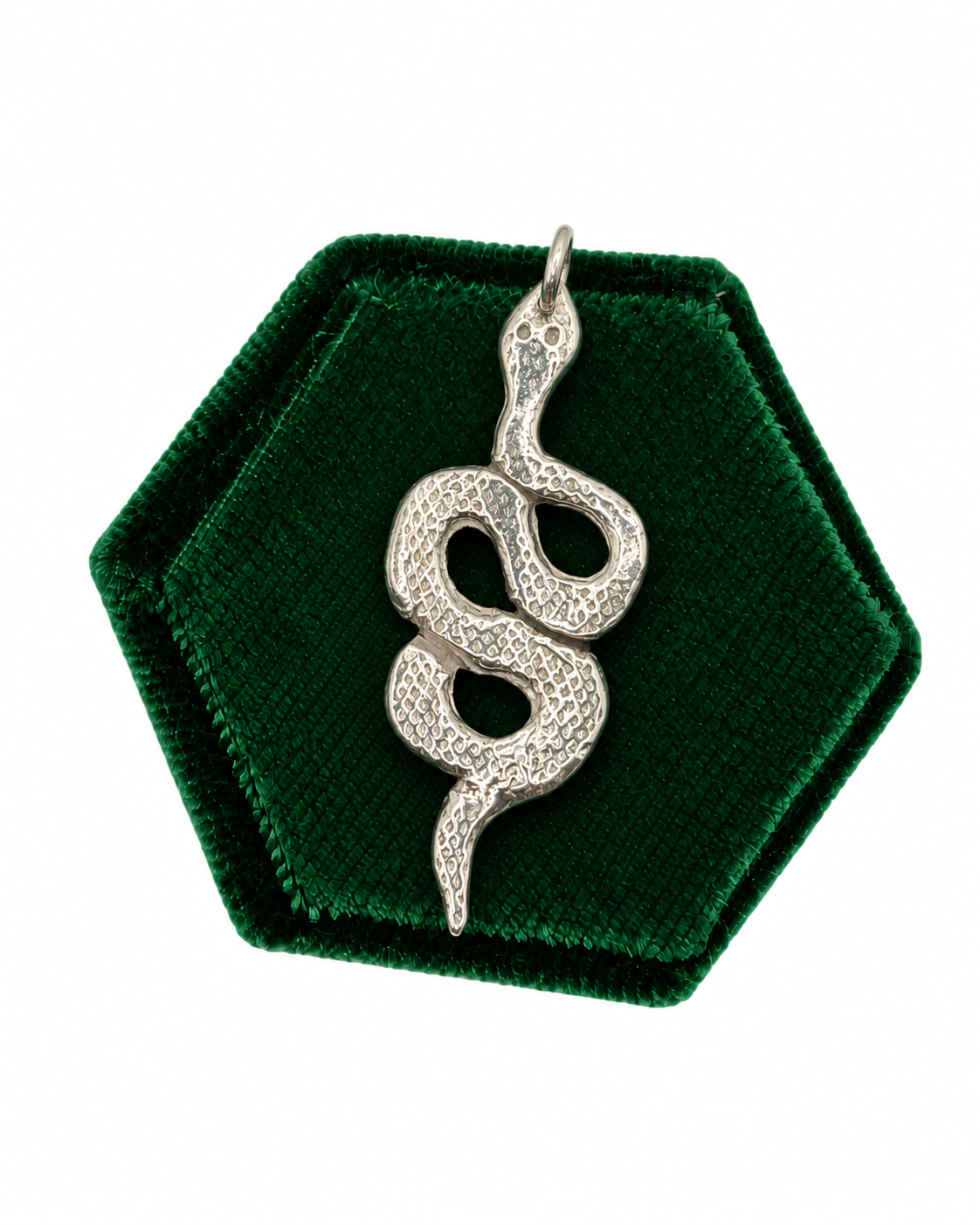 Handmade sterling silver snake charm with intricate textured scales, crafted from recycled silver and displayed on a deep green velvet jewellery cushion by Wild One Jewellery.