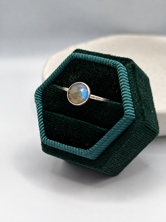 Handcrafted recycled sterling silver labradorite ring with a round faceted gemstone showing blue and golden flashes, displayed on a speckled ceramic dish.