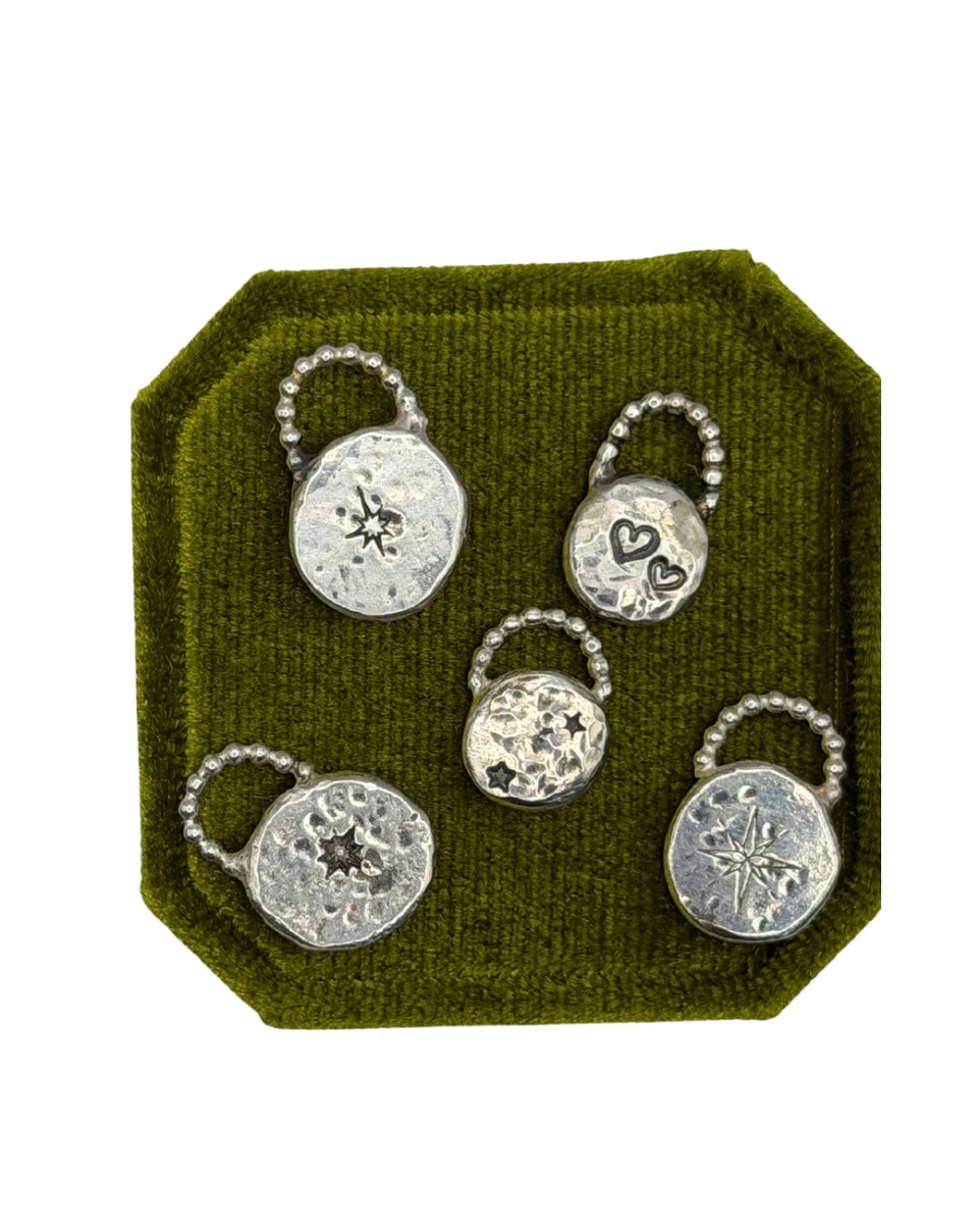 Collection of handmade Love Lock charms displayed together, featuring unique textured silver designs including tarot\-inspired symbols, celestial motifs and handstamped details\.