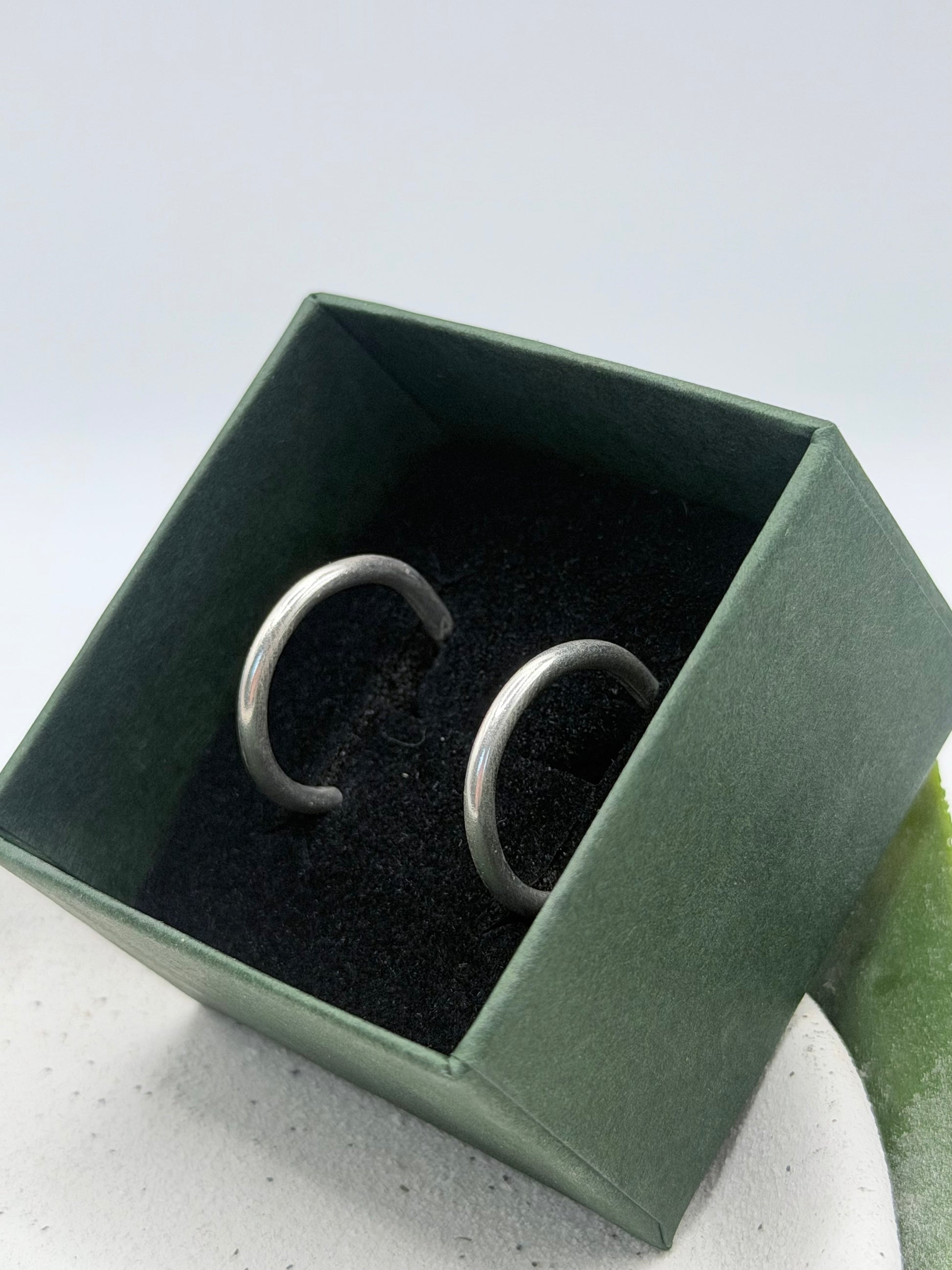 Handmade midi scroll hoop earrings crafted from solid recycled sterling silver, featuring a smooth rounded open-hoop design, photographed on a white ceramic dish by Wild One Jewellery, an independent silversmith based in Lincolnshire, UK.