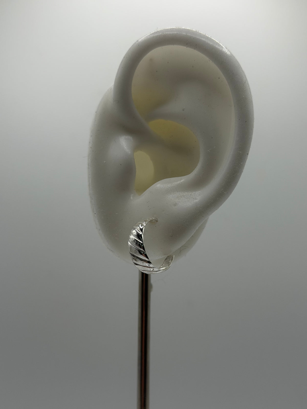 Side view of recycled sterling silver Twist Hoops showing their curved shape and raised diagonal pattern.