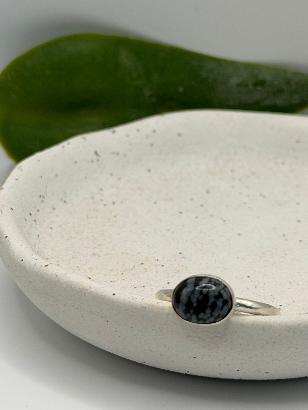 One-of-a-kind mini faceted snowflake obsidian ring from the Stone + Silver collection by Wild One Jewellery, featuring an oval black gemstone with pale snowflake-like markings set on a textured sterling silver pebble band.