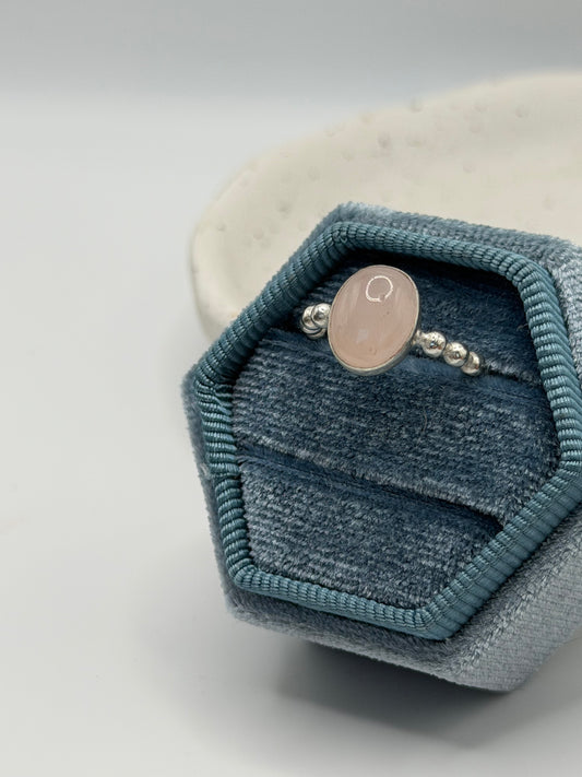 A One-of-a-kind rose quartz bobble ring from the Stone + Silver collection by Wild One Jewellery, featuring a pale pink oval cabochon set in a sterling silver band with decorative silver bobble details, displayed in a blue velvet ring box.