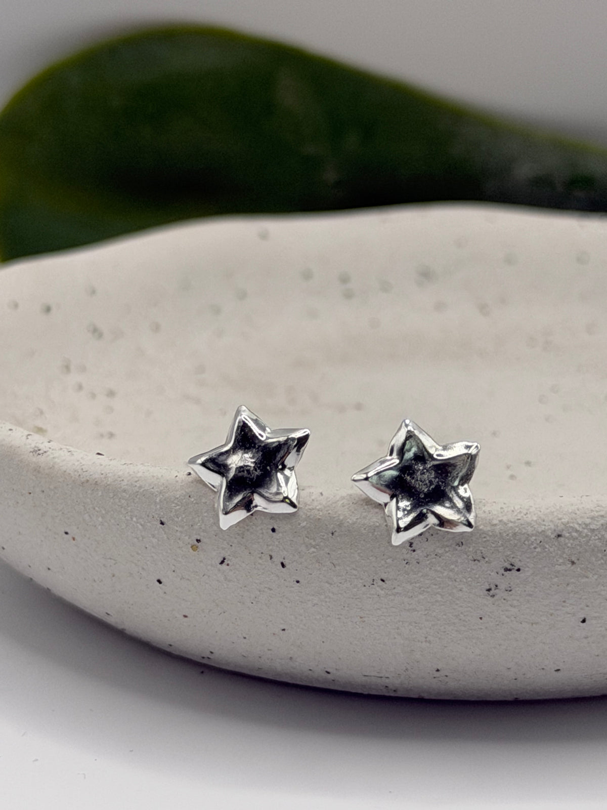 Close-up of sculptural sterling silver star studs showing their raised edges and textured finish.